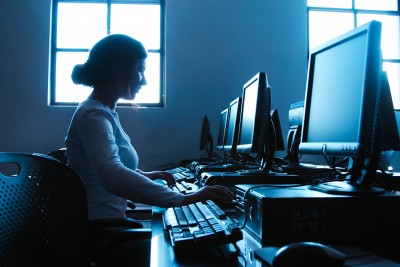 A woman works alone in front of a computer at an empty office. 