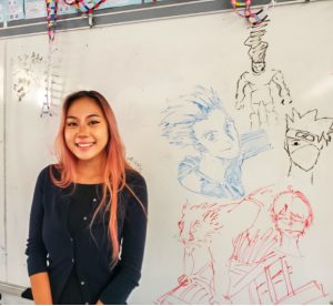 Ms. Pang poses next to whiteboard drawings of anime characters done by her students. Pang, whose favorite anime are Attack on Titan and Demon Slayer, loves sharing this interest with her students and letting them express themselves through their art. Photo by Lily Washburn. 