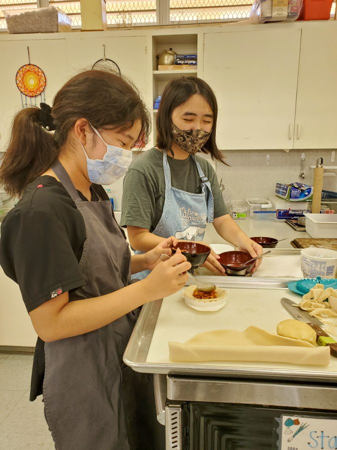 Kiana Mizuno (10) and Rylee Umakoshi (11) fold apples into mini homemade pie crusts in Culinary & Nutrition class. Their teacher, Mrs. Miyoshi says that students do not use a recipe but must instead to learn to bake by taste. The students cook the Granny Smith apples in sugar, cinnamon and a little bit of lemon juice before filling their crusts. Photo by Emily Velasco. 