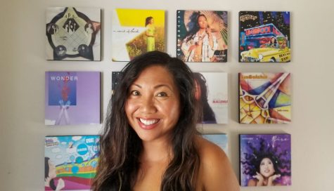 Faith Rivera stands in front of a wall with canvases of her album covers. Citing musical legends like Prince and George Micheal as her inspiration, Rivera released her first album in 1997 and continues to produce music today.