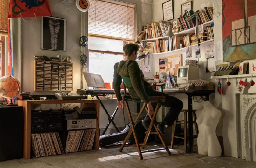 A still from the film shows Larson sitting at his Macintosh computer in his apartment struggling to write. 